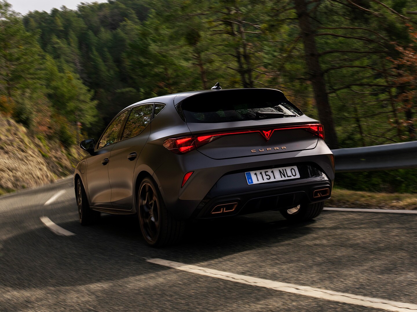 Rear-view of the CUPRA Leon riding along a road surrounded by trees.