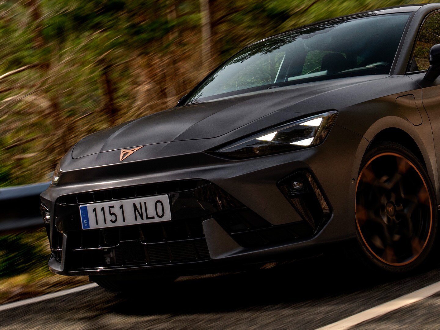 CUPRA Leon riding along a wooded road, showcasing its front design.