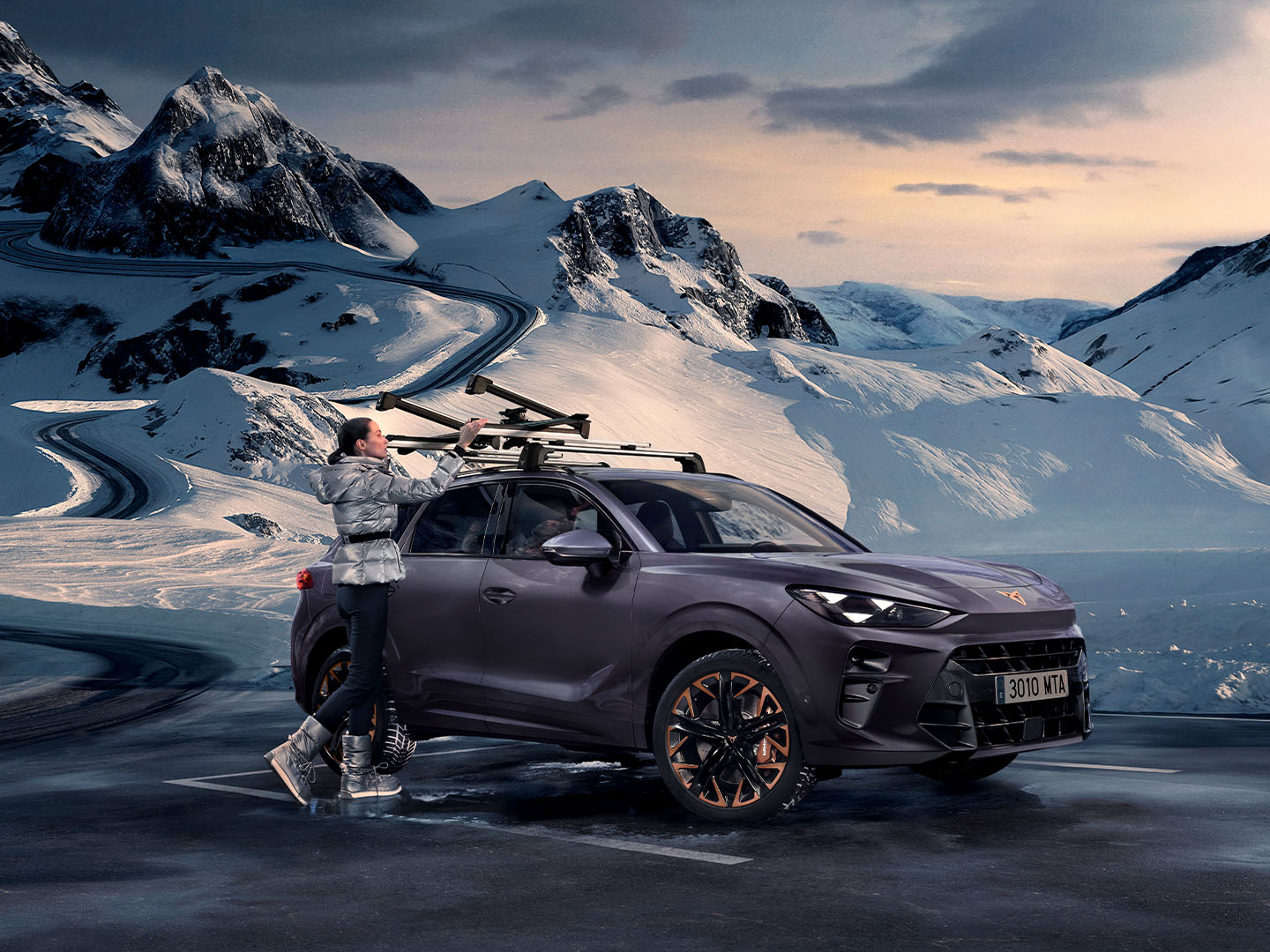 CUPRA Terramar in a snowy backdrop, showcasing the ski rack, one of its transport accessories, assembled on the roof. There is a woman using this rack for transporting its skis