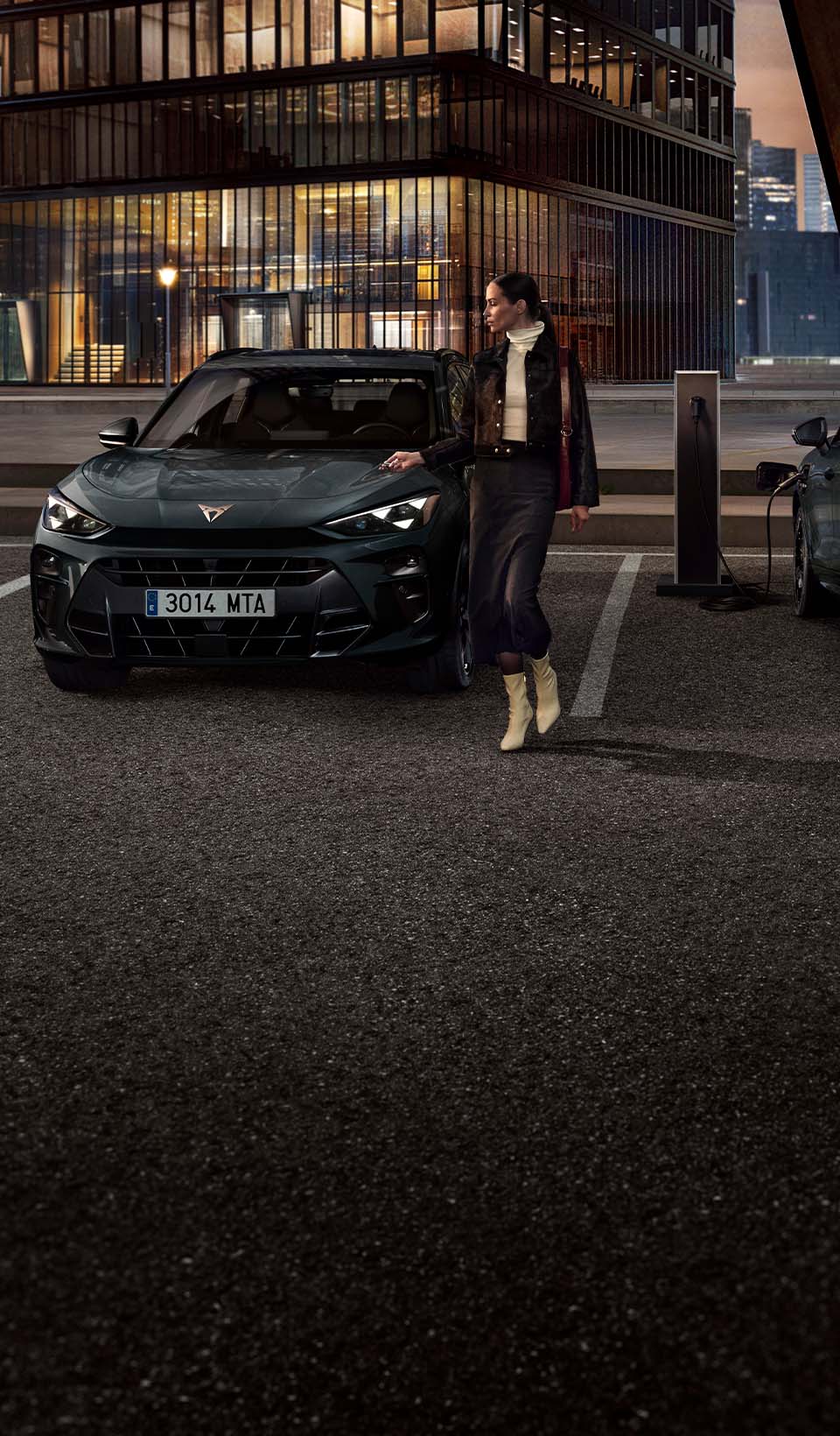 Back view of a dark grey CUPRA Leon facing a coastal city skyline at sunset.
